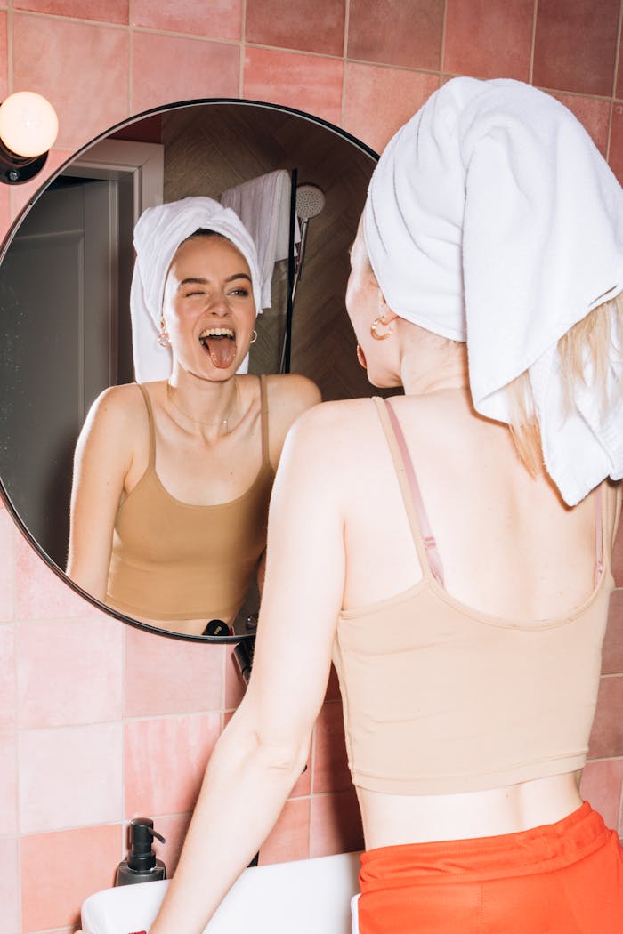 A young woman with a towel on her head makes a funny expression in a bathroom mirror.
